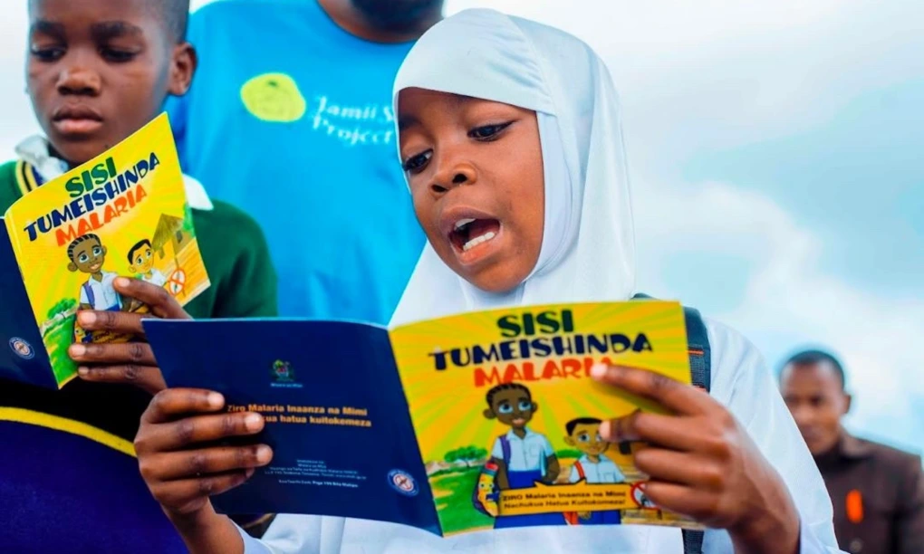 Young girl student in white hijab reading aloud from a Malaria campaign brochure