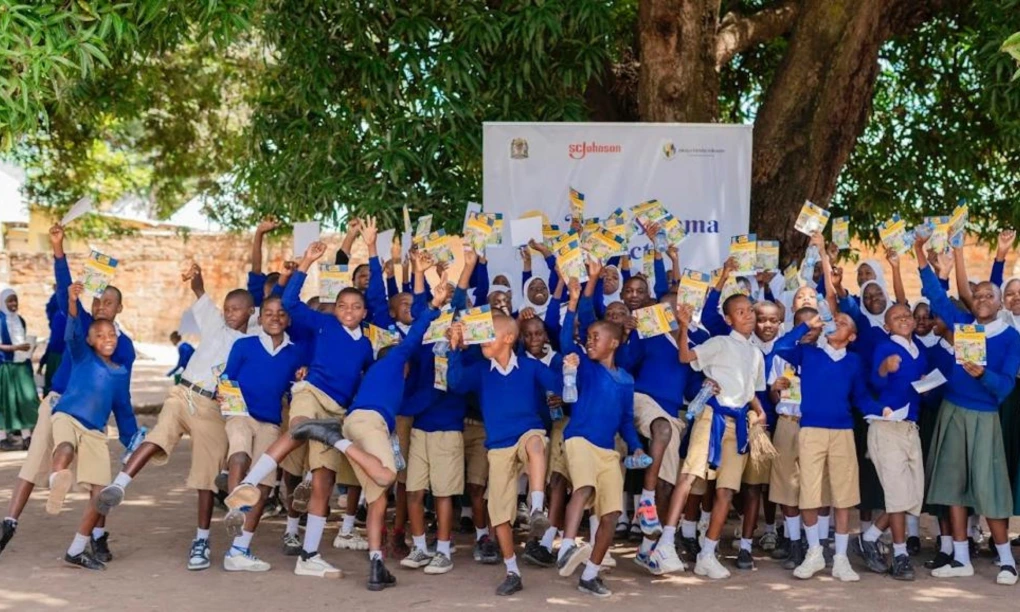 Young students in khaki shorts and blue sweaters cheering on a group photo